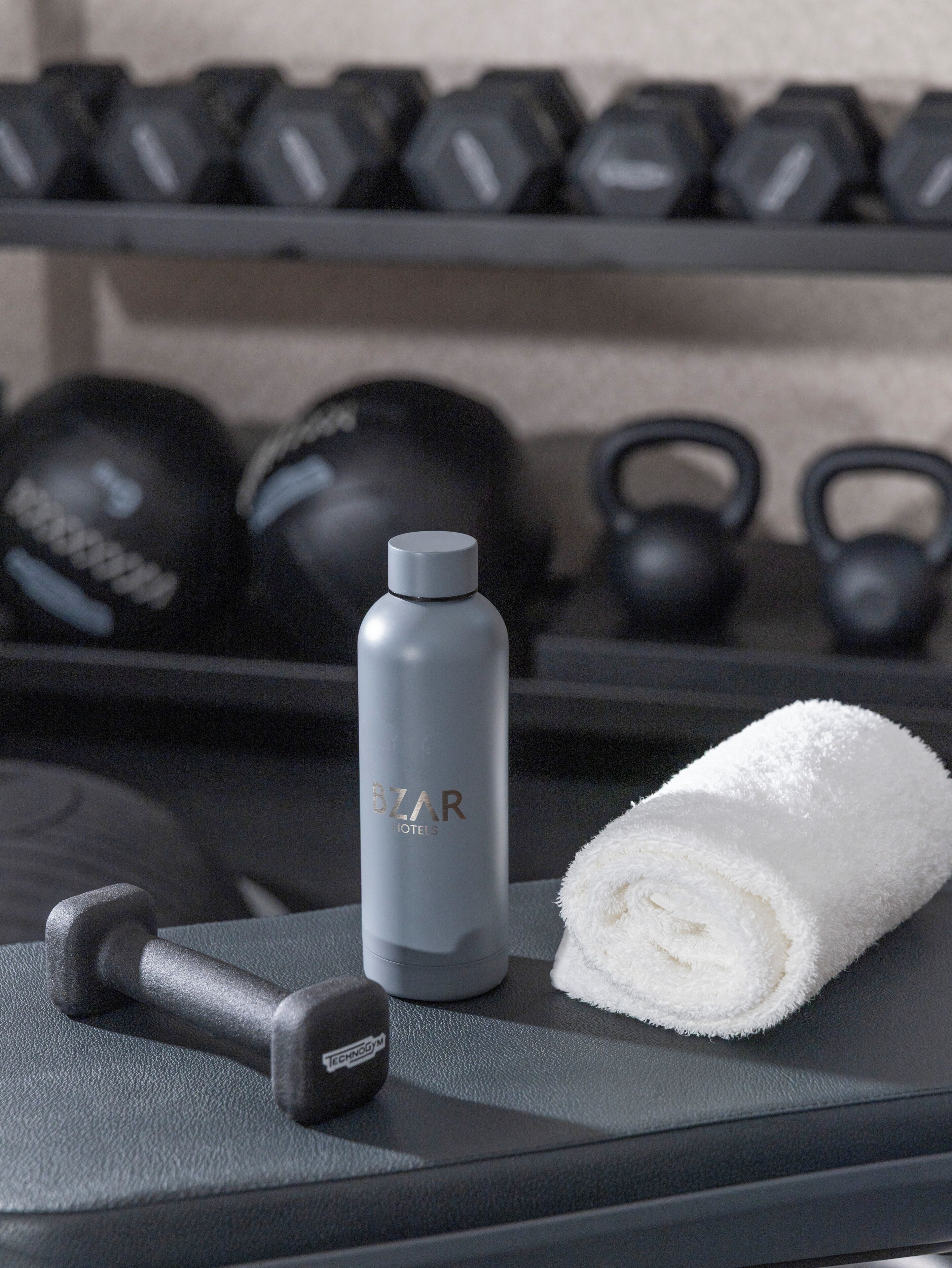 A gym with a water bottle, a towel, and dumbbells on a bench.
