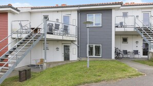 Een meerlaags woongebouw met externe trappen, genummerde kamers en een klein gazon met buitenmeubilair.