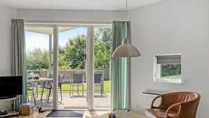 Een moderne woonkamer met een televisie, een salontafel, een fauteuil en een groot raam met gordijnen.