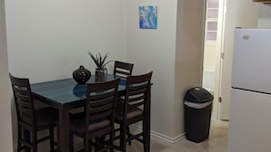 Une cuisine de taille réduite comprenant une table à manger, des chaises, une poubelle et un réfrigérateur.