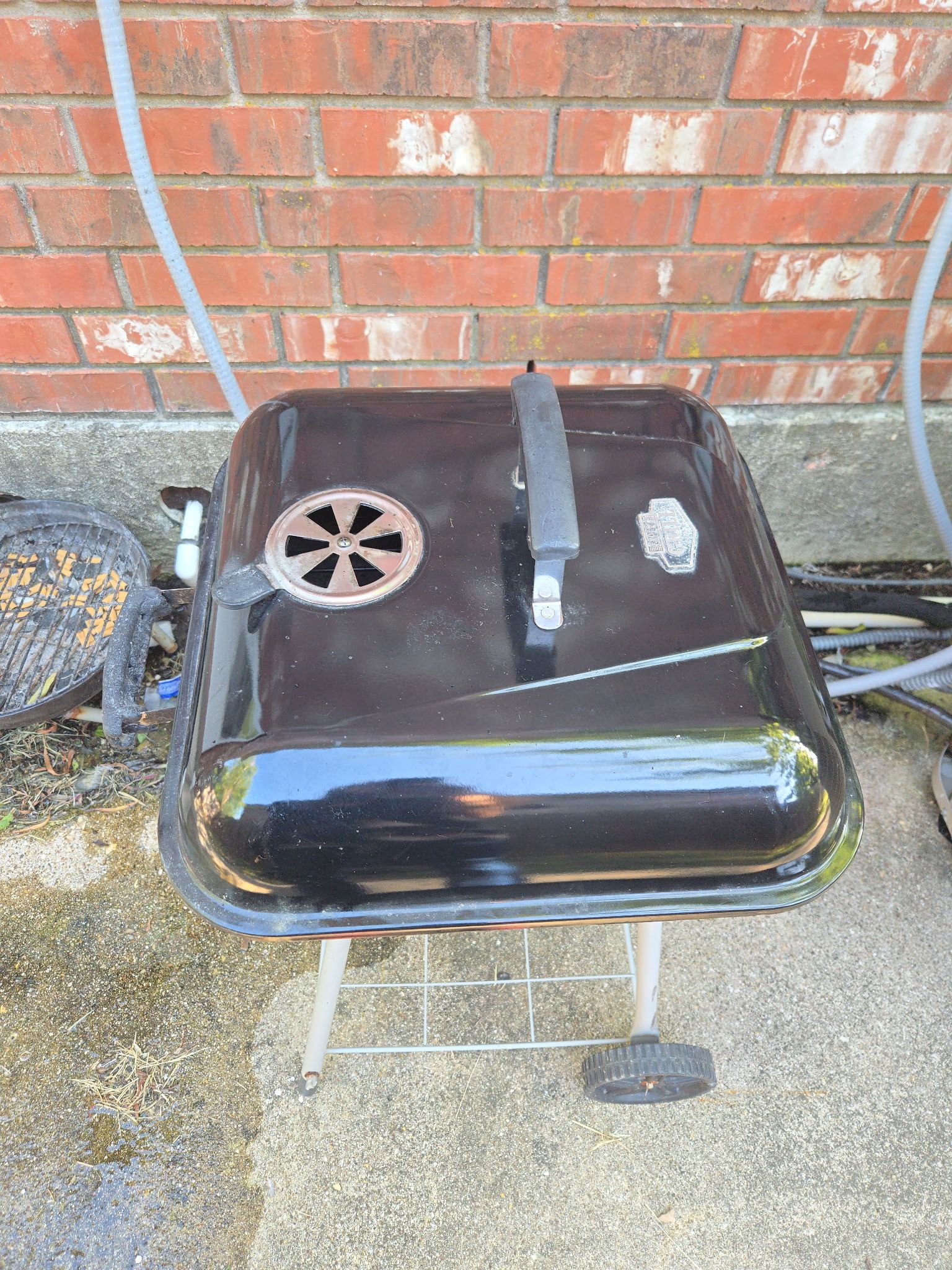 Een draagbare barbecue met ventilatie, een handvat en een metalen standaard.