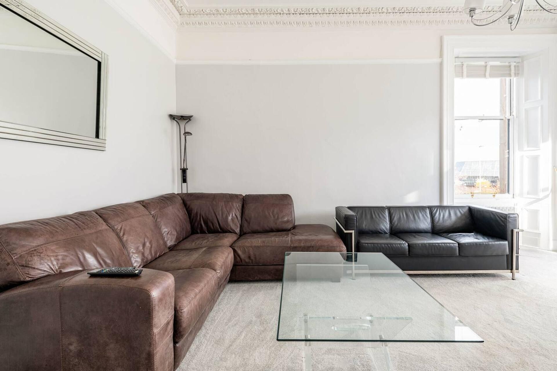 A modern living room with a brown leather sectional sofa, a glass coffee table, and a black leather sofa.