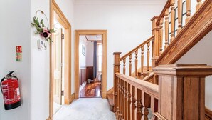 A hallway with a wooden staircase, a fire extinguisher, and a door leading to another room. - Stunning 5 Bedroom Large Apartment With Parking (Edinburgh)