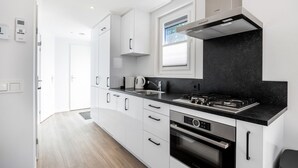 Une cuisine moderne avec des meubles blancs, un plan de travail noir, une hotte de cuisine Bosch et une fenêtre au-dessus de l’évier.