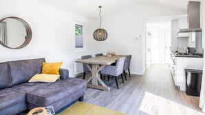 Un salon moderne avec un canapé gris, une table à manger en bois et une cuisine en arrière-plan.