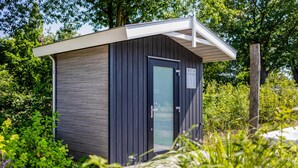 Une petite structure en bois de couleur sombre, avec un toit blanc, une porte en verre et une enseigne sur la porte.