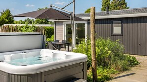 Un bain à remous avec une table et des chaises sur une terrasse, une clôture en bois et une maison dotée d’une porte-fenêtre coulissante.