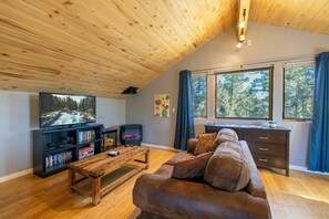A cozy living room with a wooden ceiling, a large TV, a fireplace, a sofa, and a desk with a window view. - Cozy Durango Basecamp (Durango)