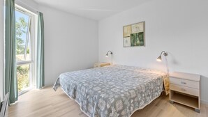 Ein Schlafzimmer mit Bett, Nachttischen, einer Wandlampe und einem Fenster mit Vorhängen.