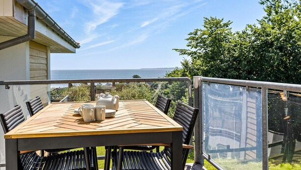 Ein Holztisch mit Stühlen auf einem Balkon mit Meerblick.