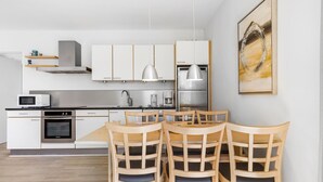 Eine moderne Küche mit weißen Schränken, einer Mikrowelle, einem Herd und einer Kaffeemaschine. Vier Holzstühle mit Kissen sind ebenfalls vorhanden.