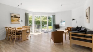 Ein modernes Wohnzimmer mit Essbereich, einer Couch, einem Fernseher und einem Balkon mit Blick ins Grüne.