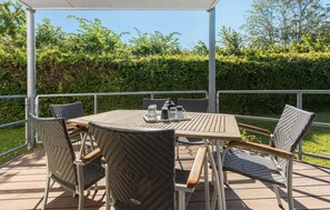 Une terrasse extérieure couverte, avec une table ronde et quatre chaises en osier.