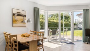 Ein Essbereich mit Holztisch und -stühlen, einem Gemälde an der Wand und Blick auf einen Garten durch große Glasüren.
