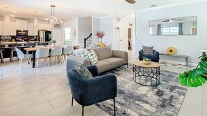 A modern living room with a sofa, coffee table, and chairs. There is a dining area with a table and chairs. A ceiling fan is visible. - Storey Lake Amazing Water view, Game Room, Movie Room and Theme Rooms (Kissimmee)