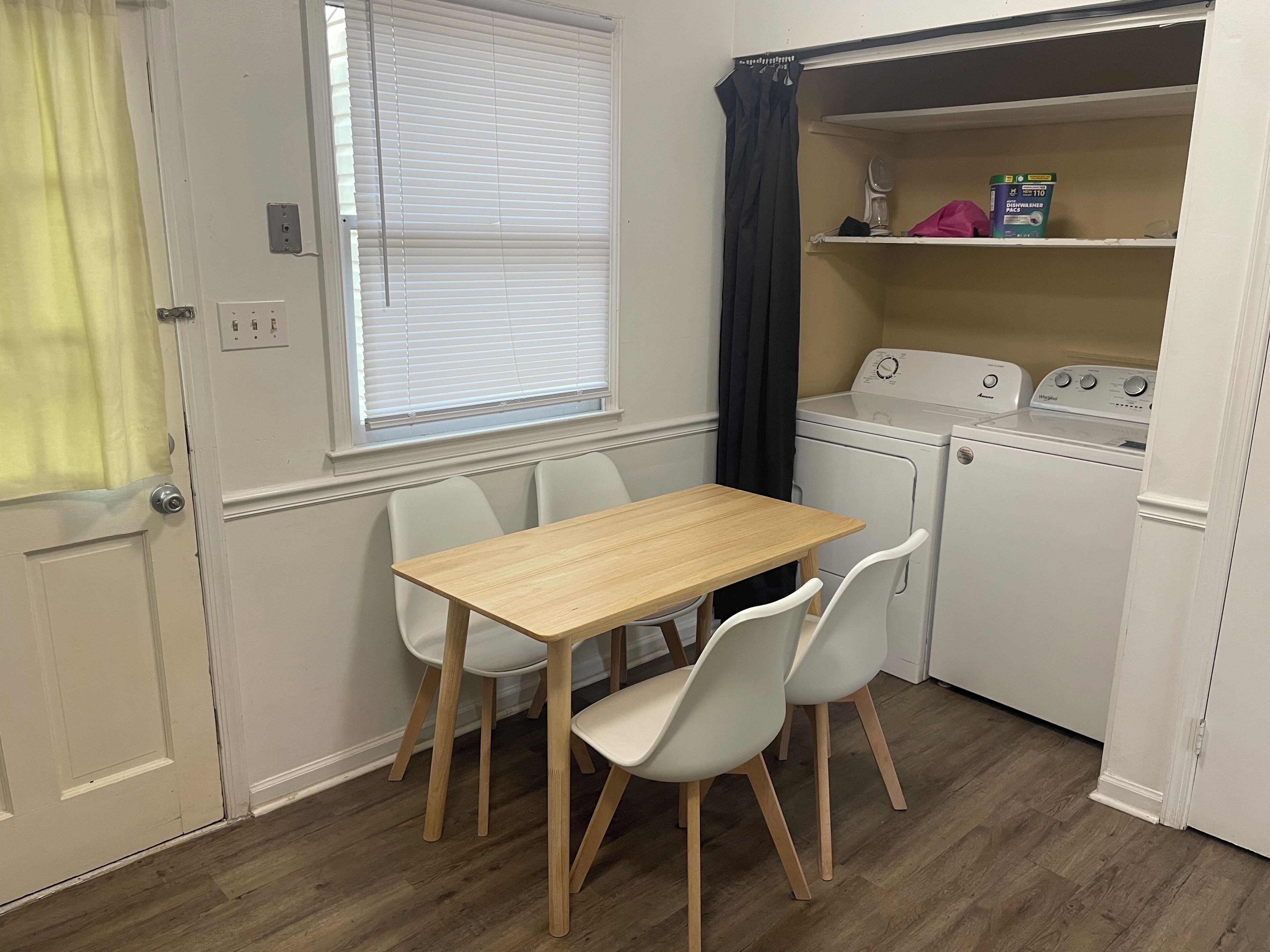 Une cuisine compacte avec une table et des chaises en bois, un lave-linge et une étagère contenant une boîte de lessive.
