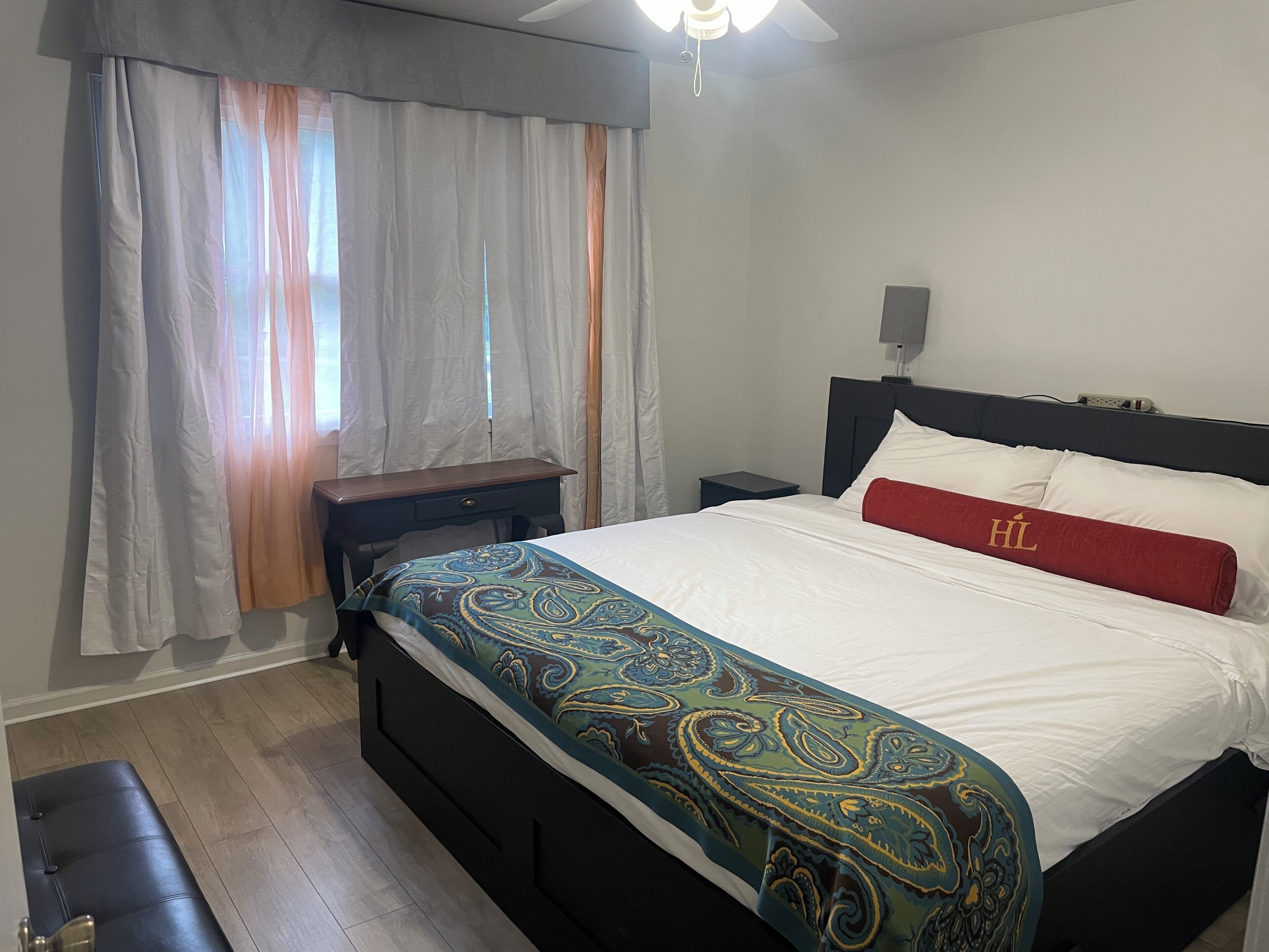 Habitación de hotel con cama, mesita de noche, escritorio y ventana con cortinas.