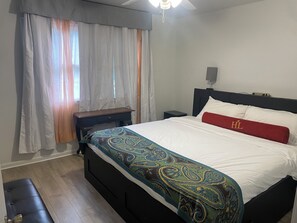 A hotel room with a bed, a nightstand, a desk, and a window with curtains.