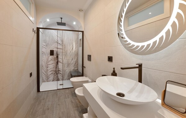 Un baño moderno con cabina de ducha de vidrio, un lavamanos ovalado grande y un espejo con diseño de hojas.