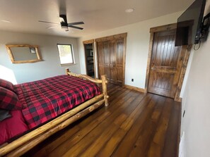 A bedroom with a wooden bed, a ceiling fan, wooden doors, and a television mounted on the wall. - Spacious, 3 bedroom private cabin on 6 acres. Near Mickelson trail & Deadwood (Lead)