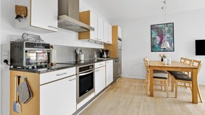 Eine moderne Küche mit weißen Schränken, einem eingebauten Backofen und einem Essbereich mit Holztisch und -stühlen.