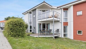 Ein zweistöckiges Wohngebäude mit Balkon, gepflasterter Auffahrt und einer Rasenfläche mit Blumen.