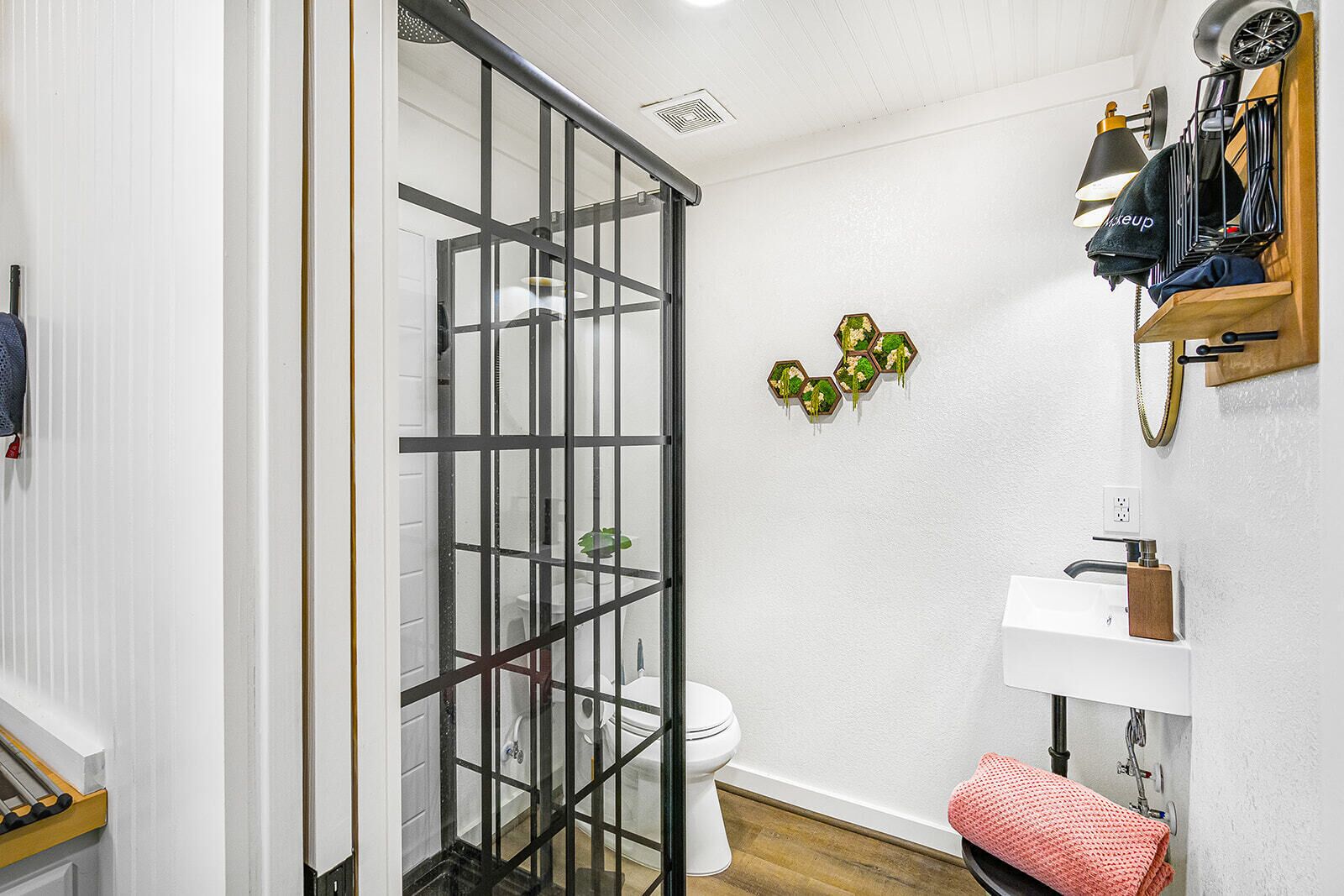Une salle de bain avec une douche à parois de verre, des toilettes, un lavabo avec un porte-savon en bois et un porte-serviettes sur lequel est posée une serviette.