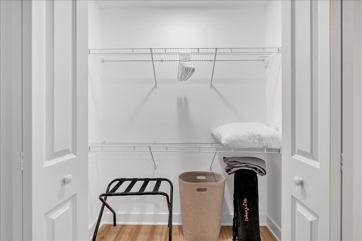 Een kleine, witte kast met een metalen kledingrek, een houten stoel en een opbergbak.