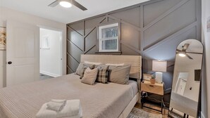Een slaapkamer met een bed, een plafondventilator, een nachtkastje met een lamp en een spiegel.