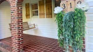 A brick porch with a swing, a wooden number '310' sign, and green foliage decorations.