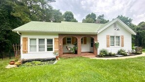 A single-story house with a green metal roof, a brick porch, and a small front yard with a lawn and a flower bed.