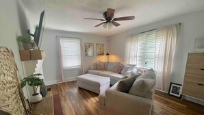 A living room with a sofa, ottoman, and a ceiling fan.