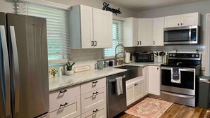 A modern kitchen with white cabinets, stainless steel appliances, a microwave, oven, and a sink.