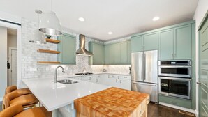 Una cucina moderna con piani di lavoro bianchi, mobili verdi ed elettrodomestici in acciaio inossidabile.