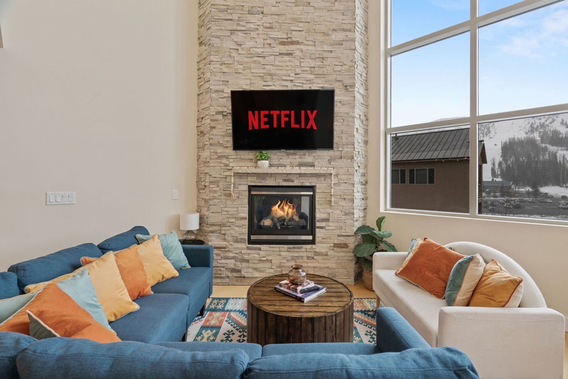 A living room with a stone fireplace, a large window, and a flat-screen TV mounted on the wall.