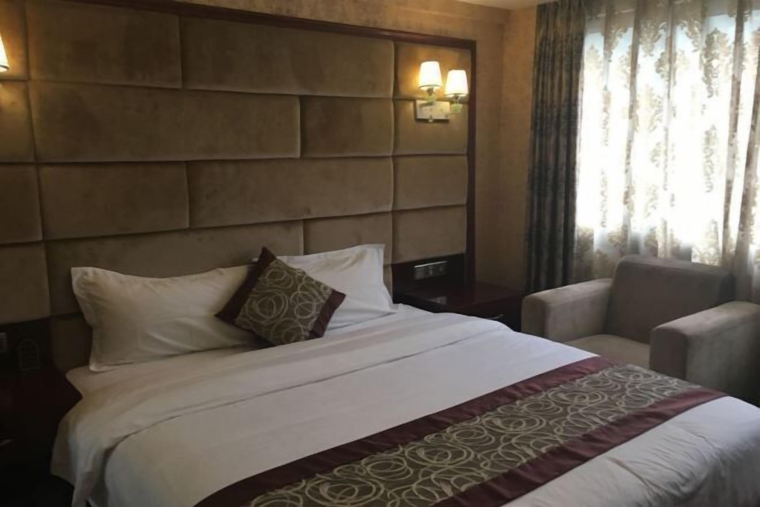 A hotel room with a large bed, a headboard with wall-mounted lights, a chair, and a window with curtains.