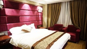 A hotel room with a large bed, red upholstered headboard, a wooden nightstand, a red armchair, and a large window with curtains. - Hongyan Business Hotel (Baoxing)