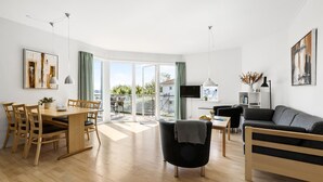 A modern living room with a dining area, a sofa, a TV, and a balcony with a view. - Gudhjem Søpark Lejl. 38 (Gudhjem)