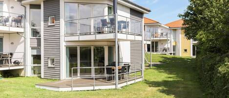 Um edifício residencial moderno, com dois andares, varanda, grandes janelas e um gramado.