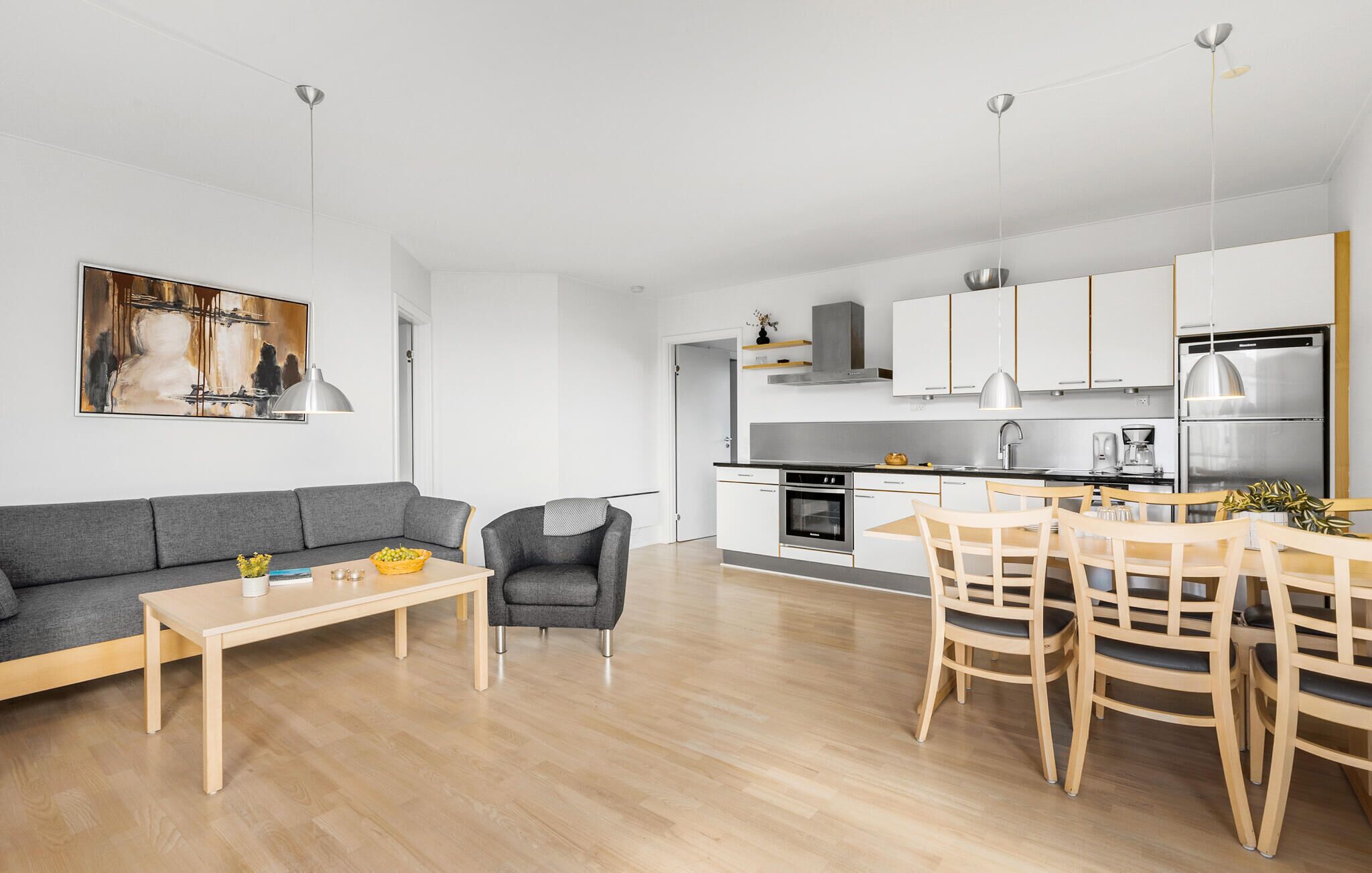 A modern kitchen with white cabinets, stainless steel appliances, and a dining area with wooden chairs and a table.