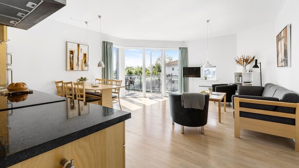 A modern apartment with a kitchen, dining area, and living room. It features a large sliding glass door to the outside, a flat-screen TV, and a sofa. - Gudhjem Søpark Lejl. 38 (Gudhjem)