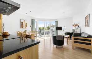 Un apartament modern amb cuina, zona de dinar i saló. Disposa d'un gran finestral corredís a l'exterior, televisió de pantalla plana i sofà.