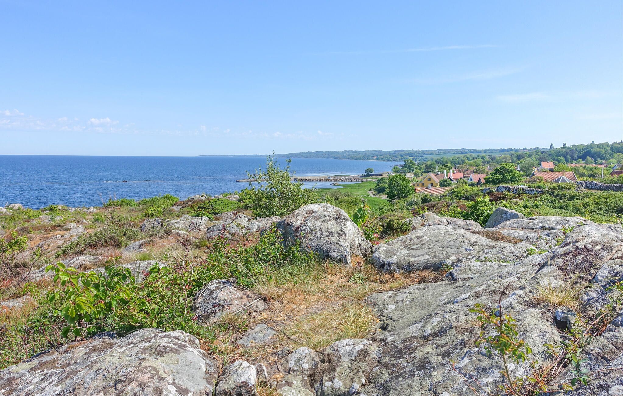 A coastal landscape with rocky terrain, greenery, and a view of the sea and distant buildings.