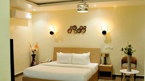 A modern hotel room with a large bed, bedside tables, a small round table, and decorative wall sconces. - THE ADDRESS HOTEL AND TOWER (Abuja)