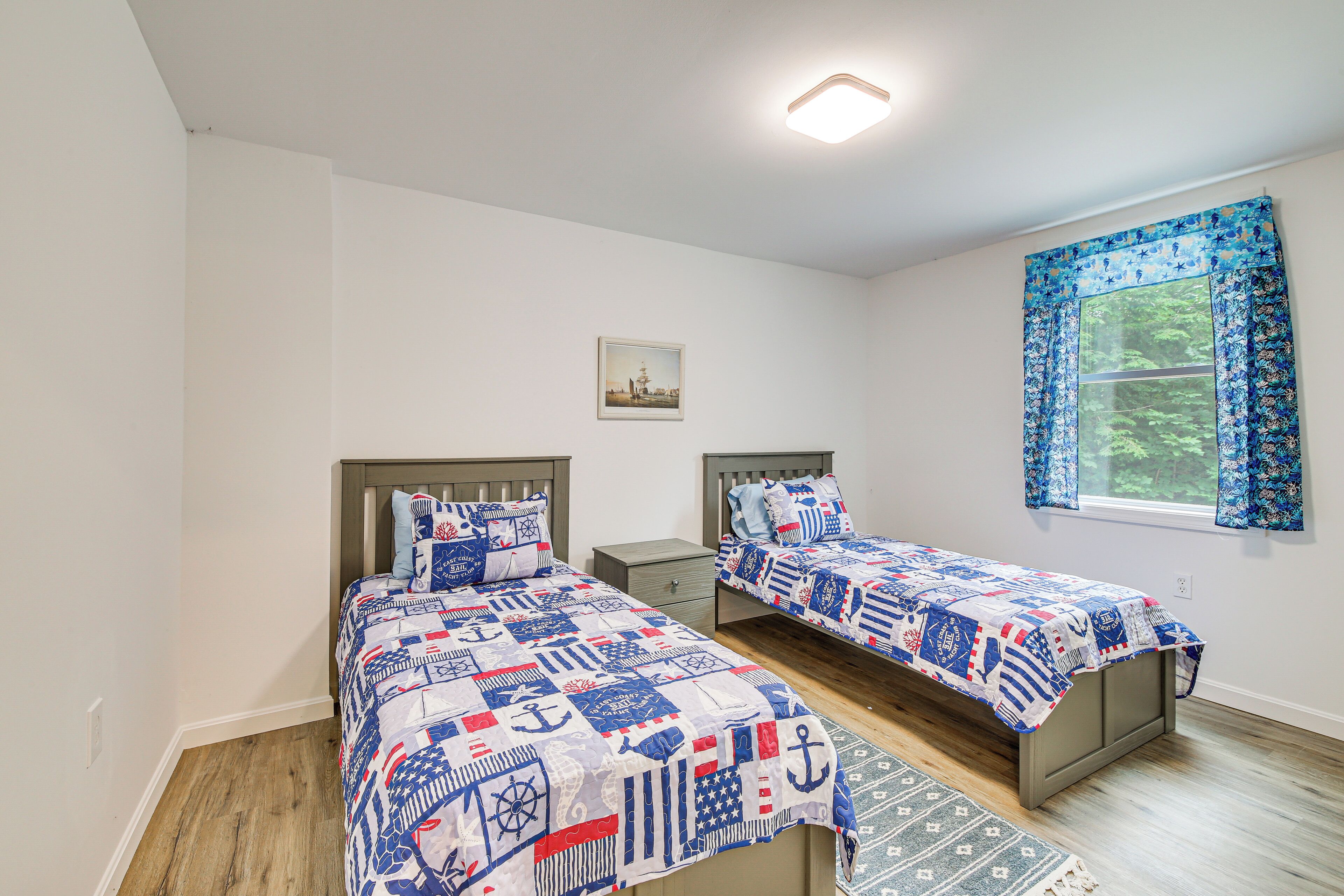 Een slaapkamer met twee bedden, een raam met gordijnen, een nachtkastje en een klein schilderij aan de muur.