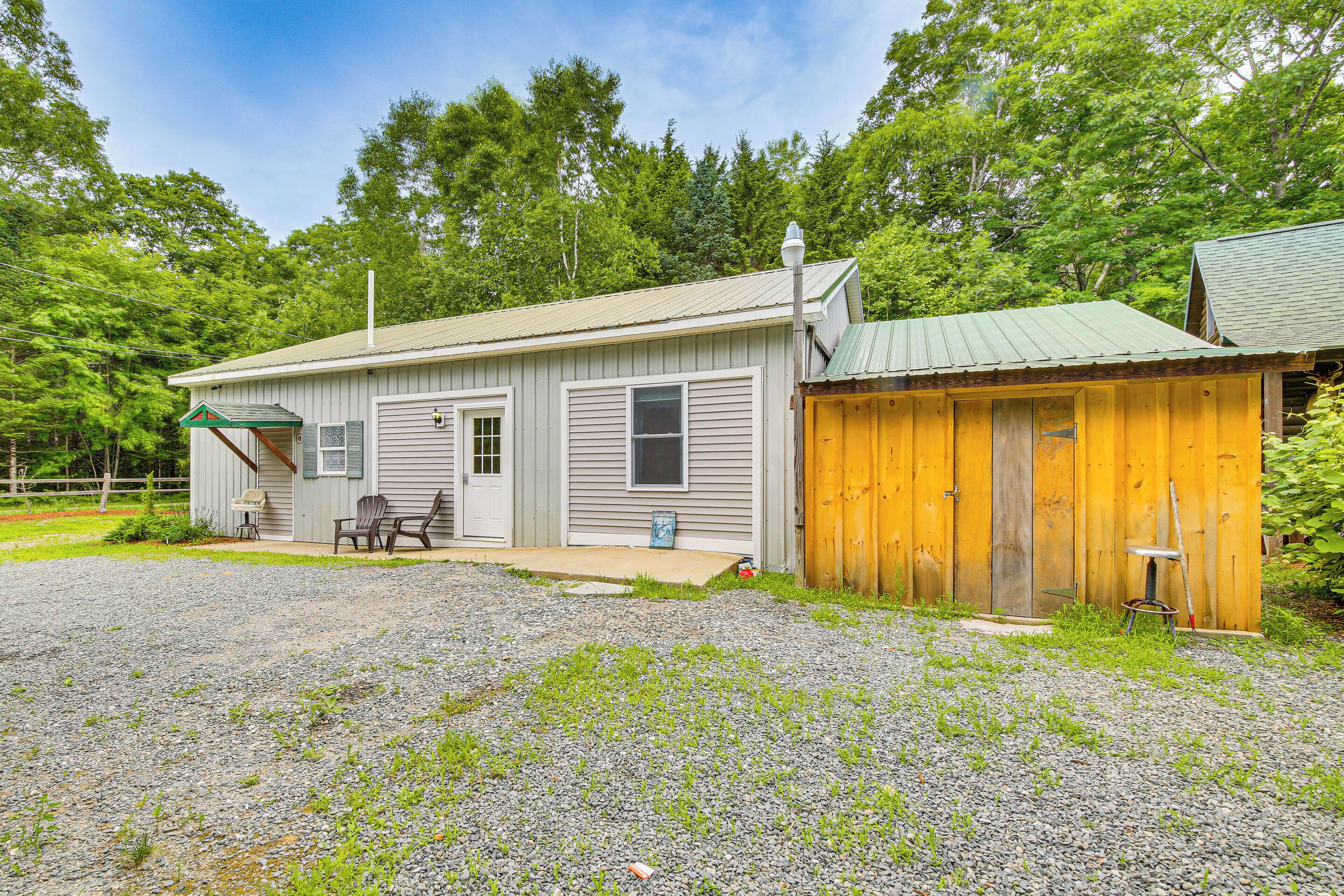 A single-story building with a gravel driveway, a covered patio area with outdoor seating, and a wooden shed.