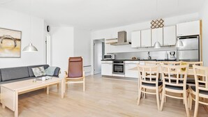 Une cuisine moderne avec des armoires blanches et des appareils en acier inoxydable. On y trouve un coin repas avec des chaises et une table en bois.