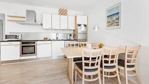 Une cuisine moderne avec des meubles blancs, des appareils en acier inoxydable et un coin repas comprenant des chaises et une table en bois.
