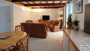 Una sala de estar con una mesa de comedor de madera, sofás de cuero, un televisor y una planta en maceta.
