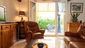 Una sala de estar con un sofá de cuero marrón, un mueble de madera, un televisor y una mesa con un bol y vasos.